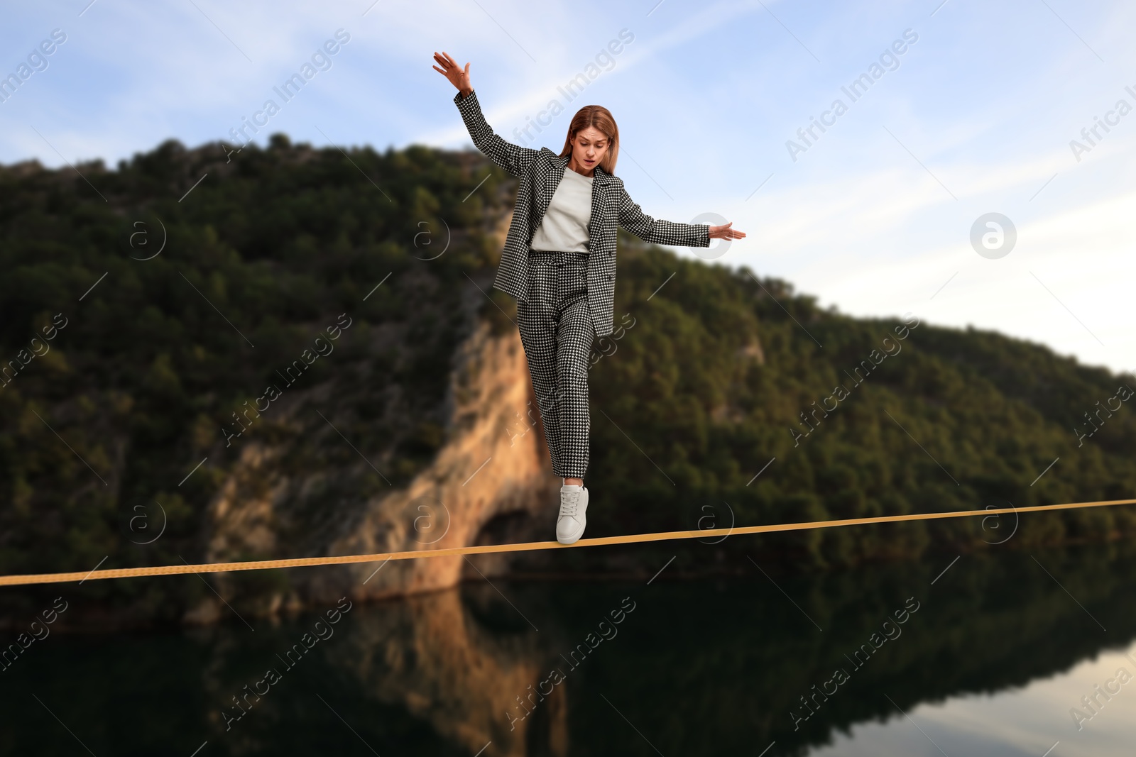 Image of Businesswoman walking rope in mountains. Concept of risk and balance