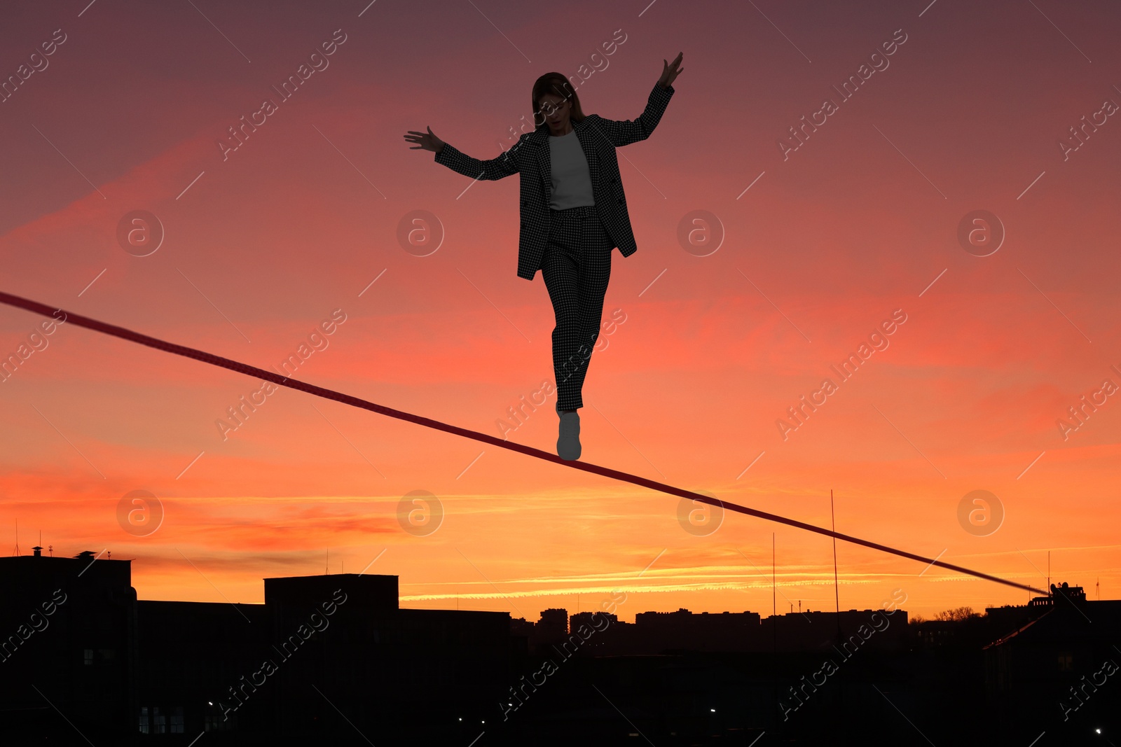 Image of Businesswoman walking rope over city at sunset. Concept of risk and balance