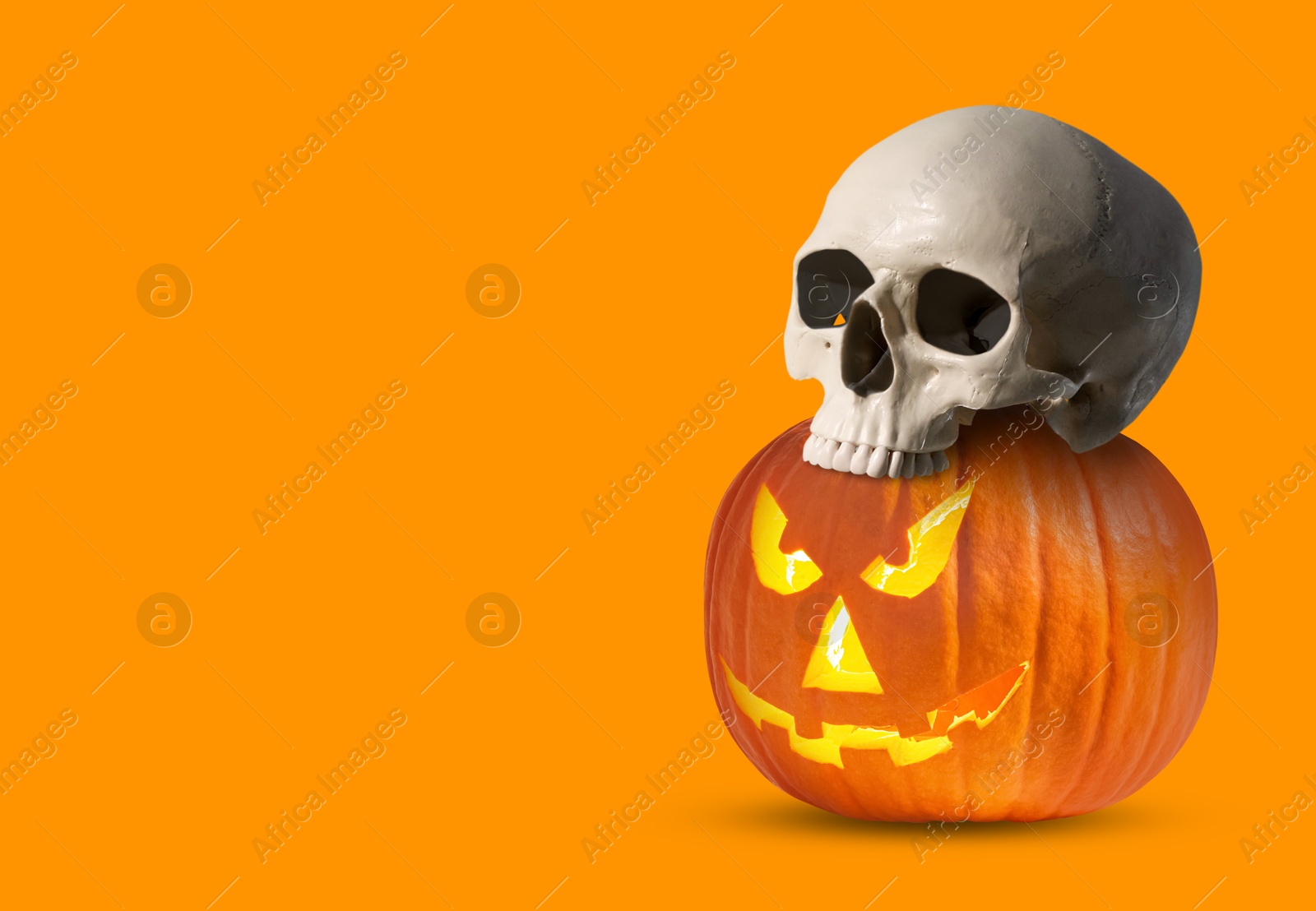 Image of Spooky glowing jack o'lantern and scary skull on orange background, space for text. Halloween celebration