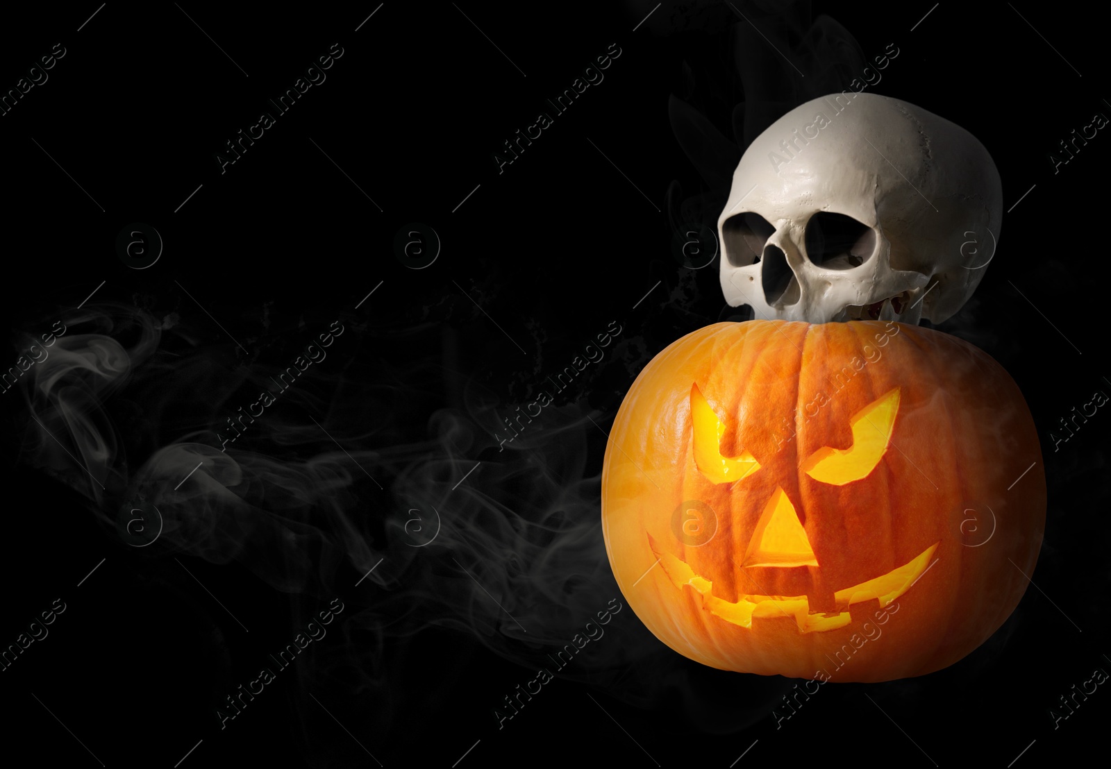 Image of Spooky glowing jack o'lantern and scary skull in smoke on black background. space for text. Halloween celebration