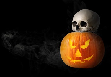 Image of Spooky glowing jack o'lantern and scary skull in smoke on black background. space for text. Halloween celebration