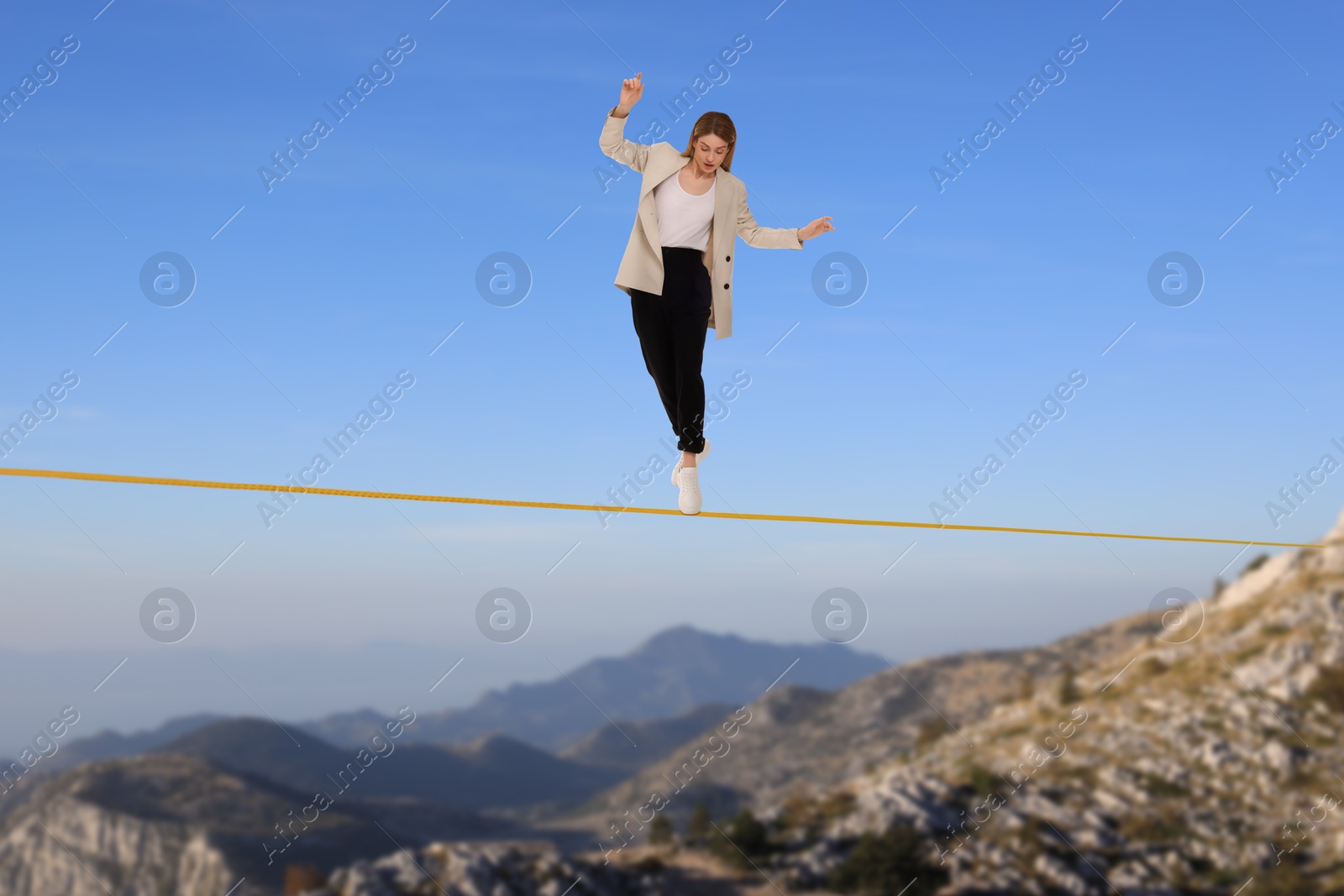 Image of Businesswoman walking rope in mountains. Concept of risk and balance