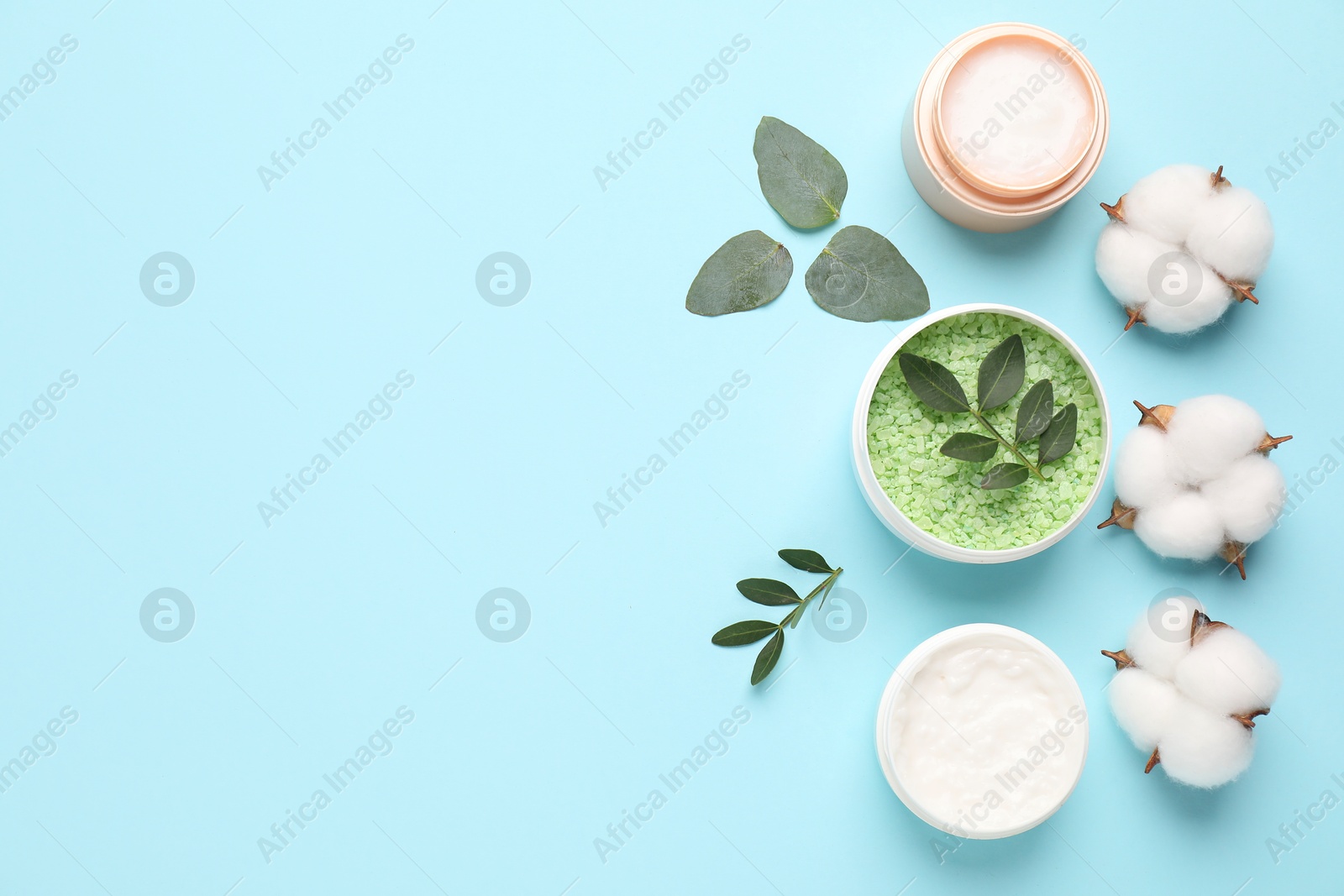 Photo of Different cosmetic products, leaves and cotton flowers on light blue background, flat lay. Space for text