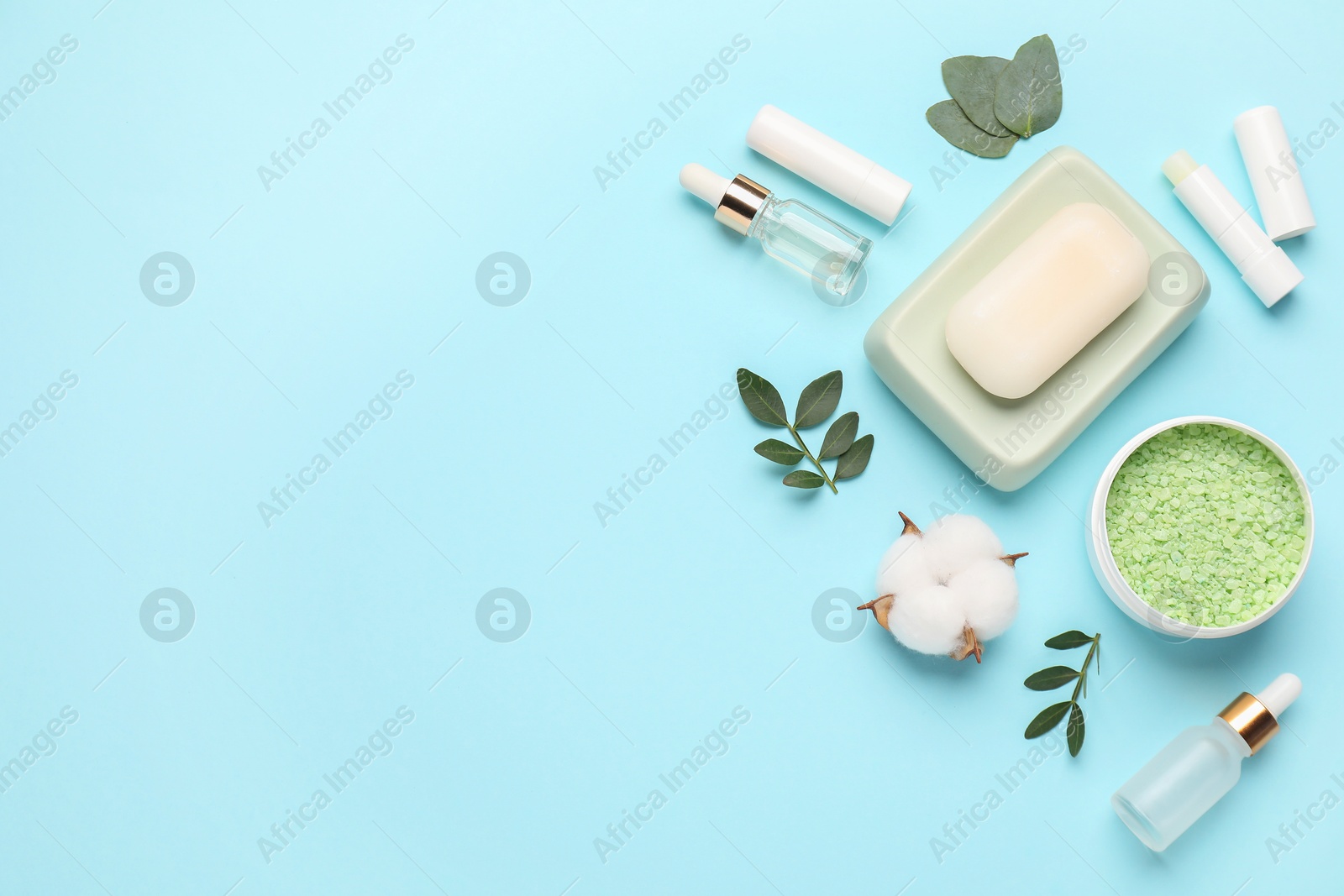 Photo of Different cosmetic products, leaves and cotton flower on light blue background, flat lay. Space for text