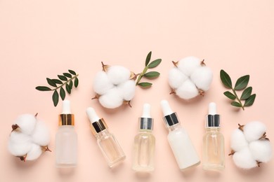 Photo of Different cosmetic products, cotton flowers and green leaves on beige background, flat lay