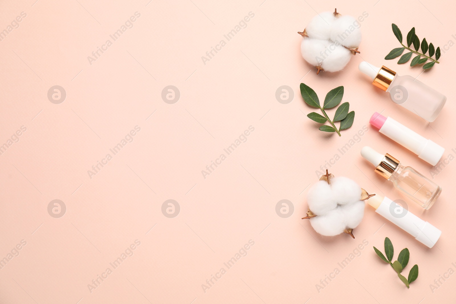 Photo of Different cosmetic products, cotton flowers and green leaves on beige background, flat lay. Space for text