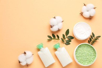 Photo of Different cosmetic products, cotton flowers and leaves on pale orange background, flat lay. Space for text