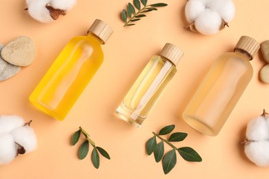 Photo of Different cosmetic products, cotton flowers and green leaves on pale orange background, flat lay