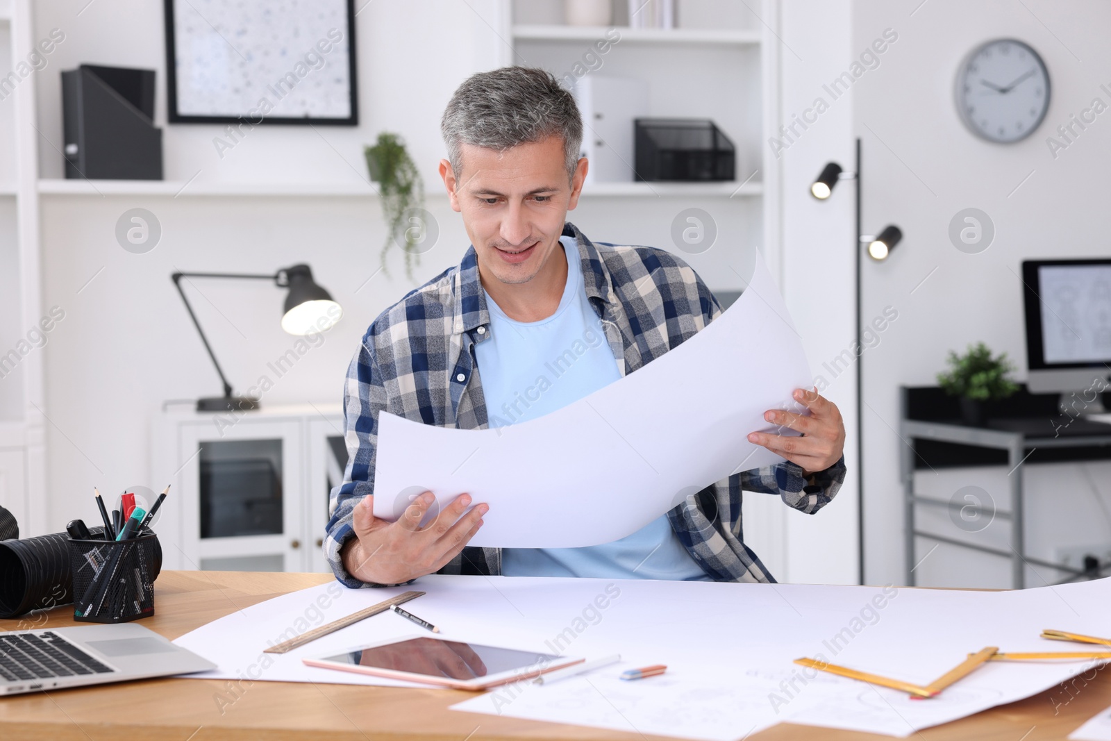 Photo of Architect checking engineering drawing at table in office