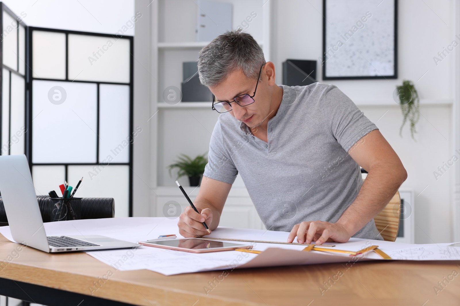 Photo of Architect making engineering drawing at wooden table in office