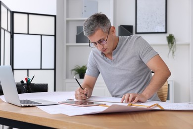 Architect making engineering drawing at wooden table in office