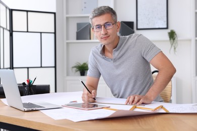 Photo of Architect with engineering drawing at wooden table in office