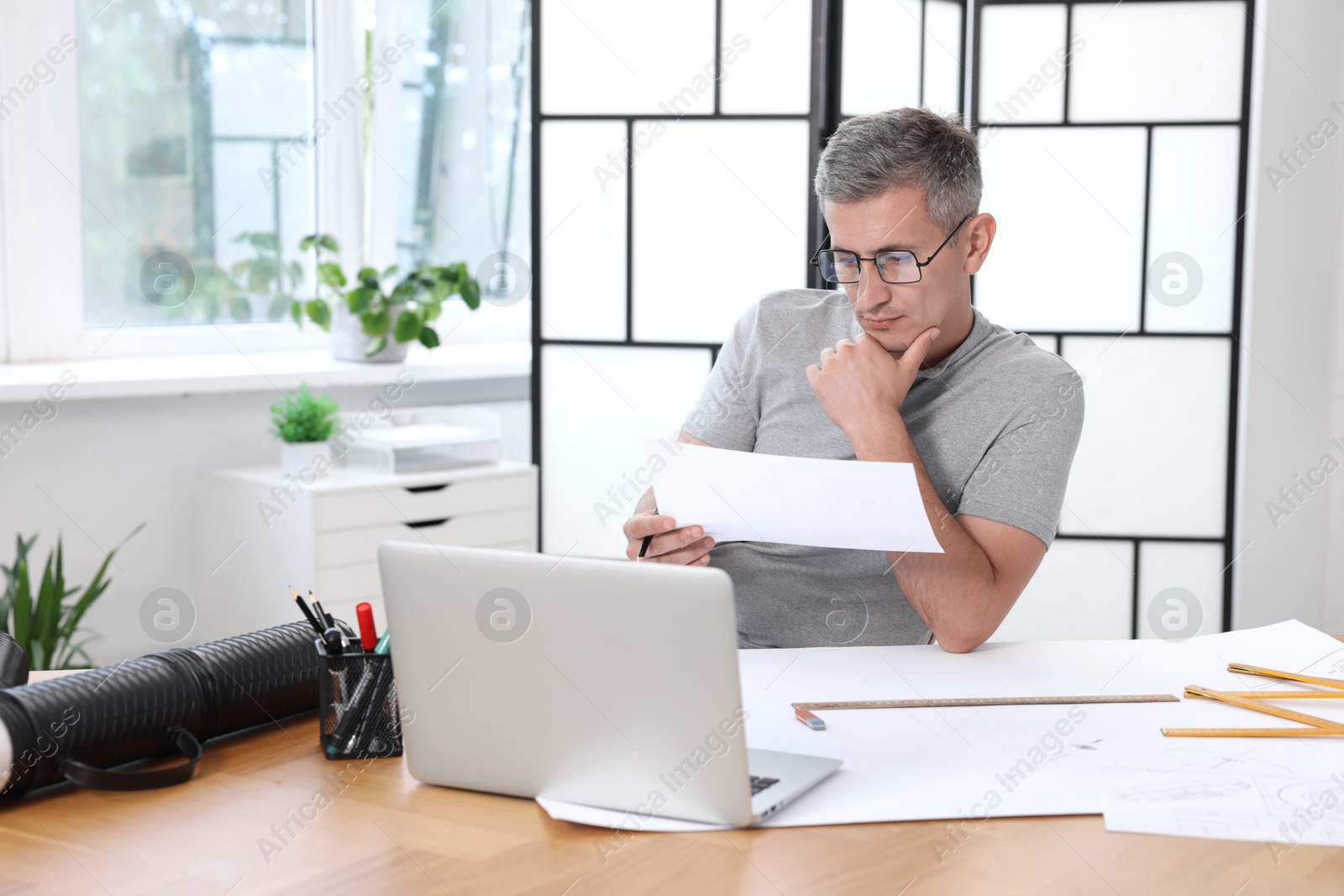 Photo of Architect with engineering drawing at wooden table in office