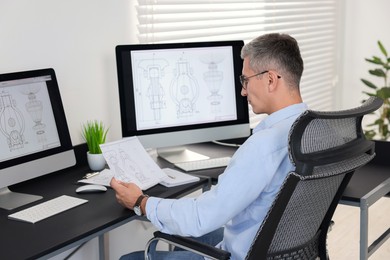 Photo of Architect checking engineering drawing at table in office