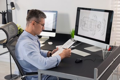 Photo of Architect checking engineering drawing at table in office