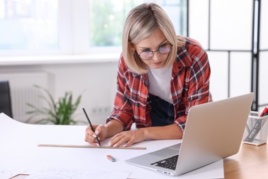 Architect making engineering drawing at wooden table in office