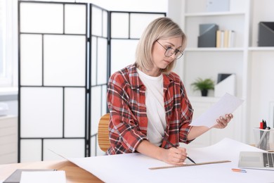 Architect with engineering drawing at table in office