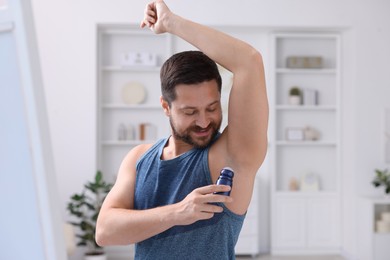 Handsome man applying roll-on deodorant at home