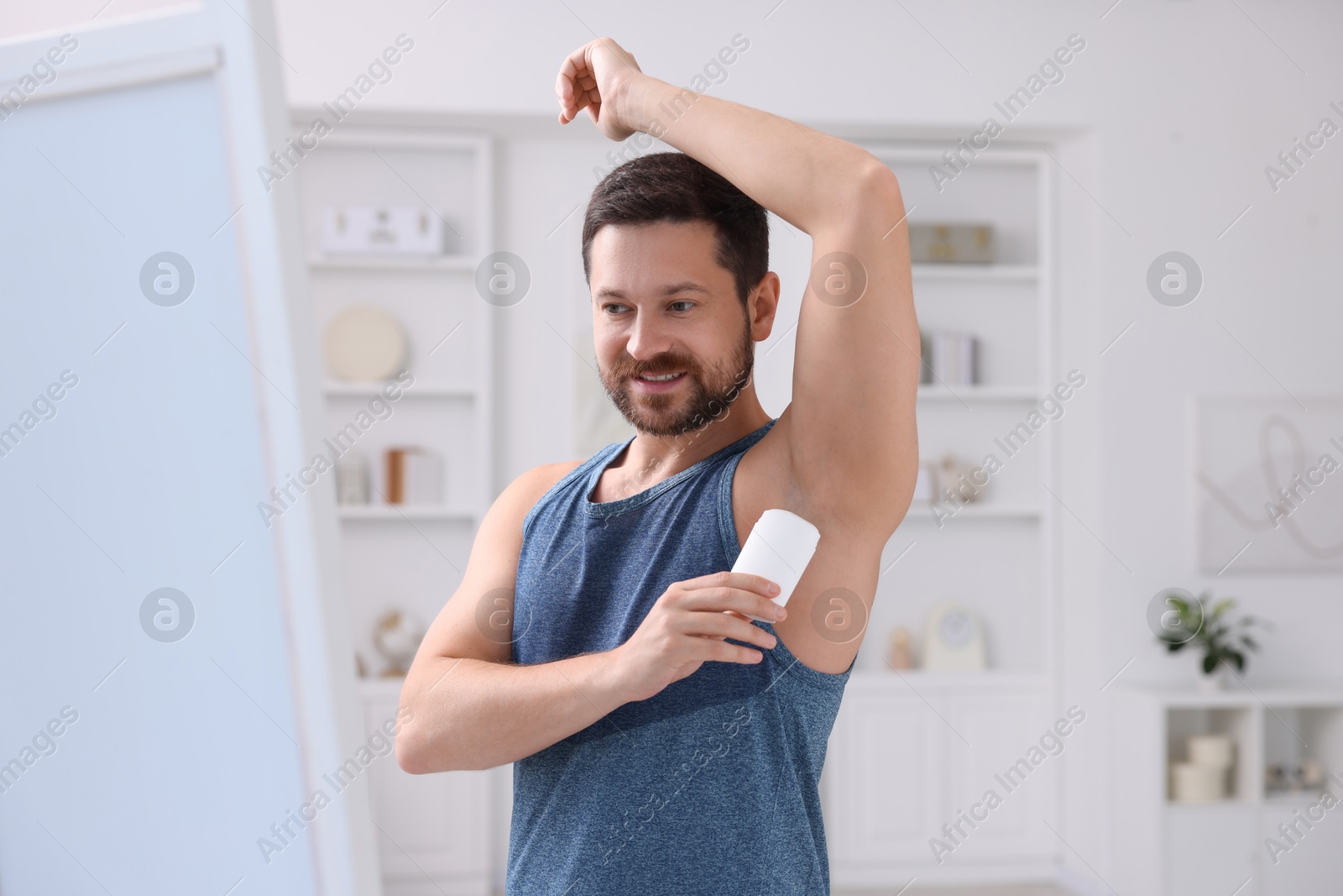 Photo of Smiling man applying solid deodorant at home