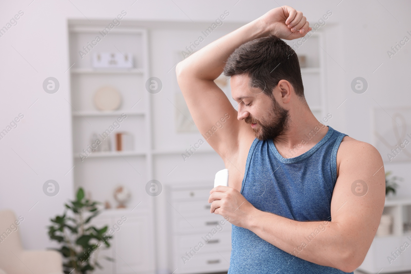 Photo of Handsome man applying solid deodorant at home. Space for text