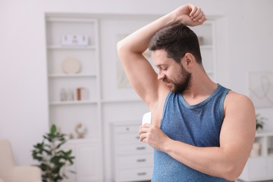 Handsome man applying solid deodorant at home. Space for text