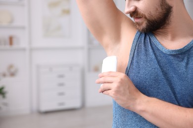 Photo of Man applying solid deodorant at home, closeup. Space for text