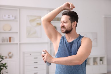 Smiling man applying spray deodorant at home. Space for text