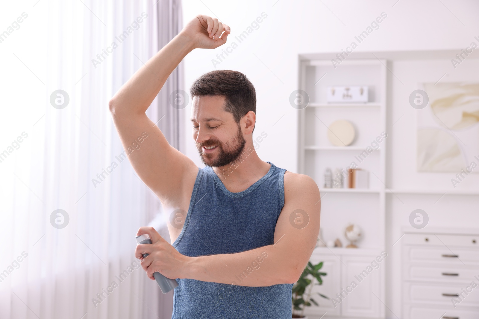 Photo of Smiling man applying spray deodorant at home