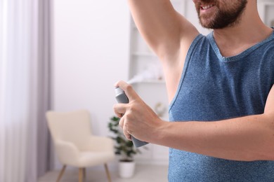 Photo of Smiling man applying spray deodorant at home, closeup. Space for text