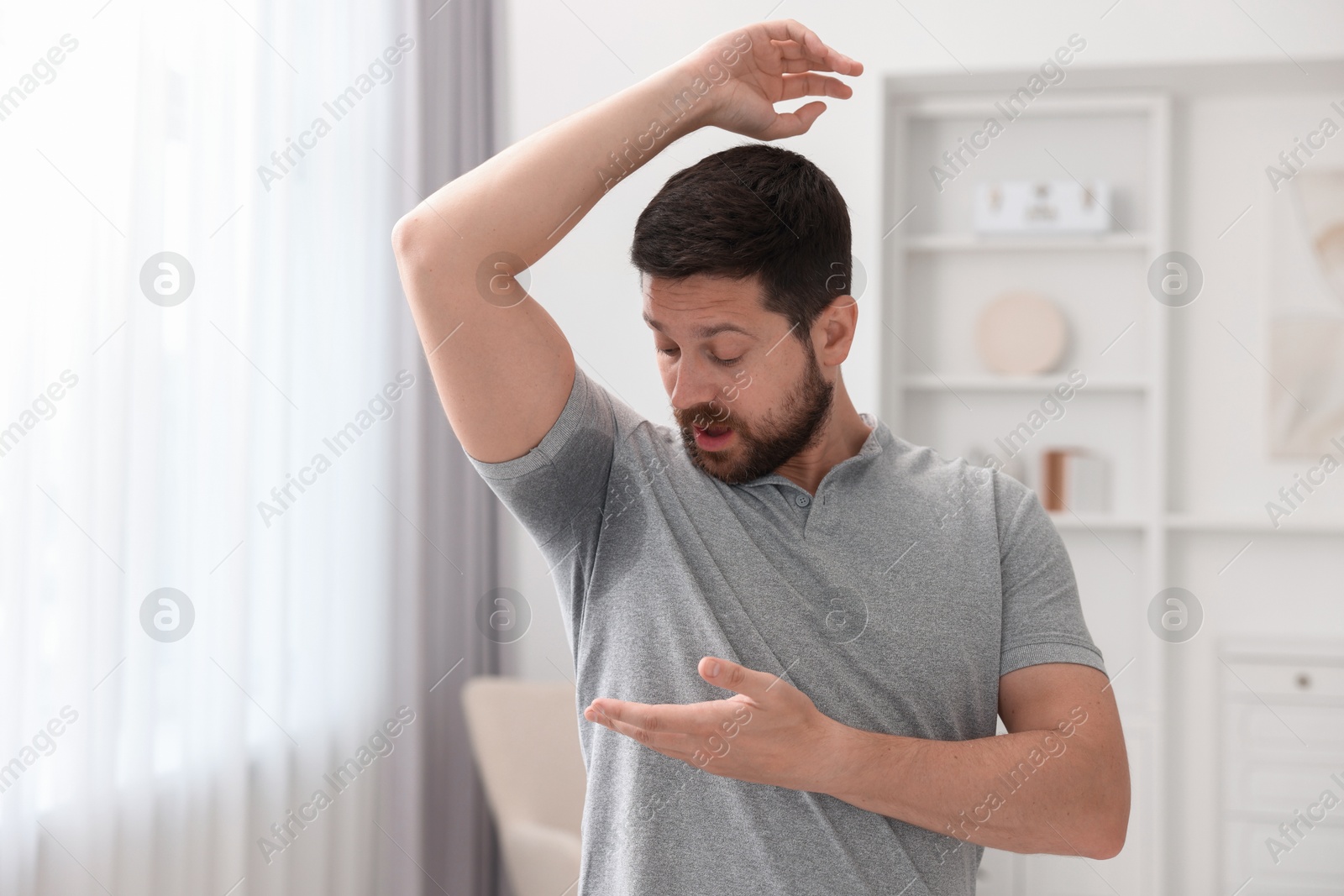 Photo of Emotional man in t-shirt before using deodorant at home