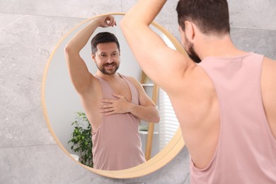 Smiling man after using deodorant near mirror at home, back view