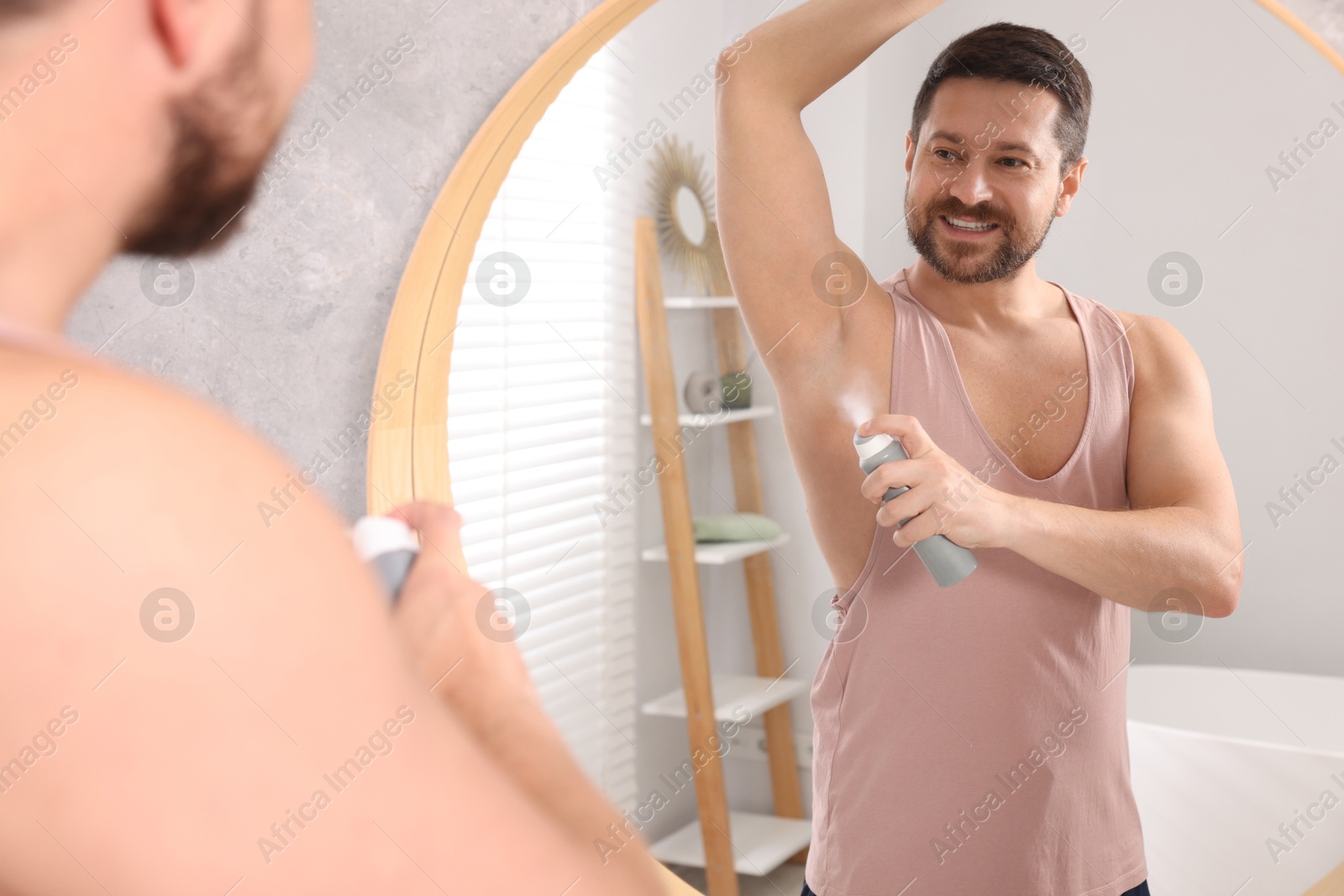 Photo of Smiling man applying spray deodorant near mirror at home