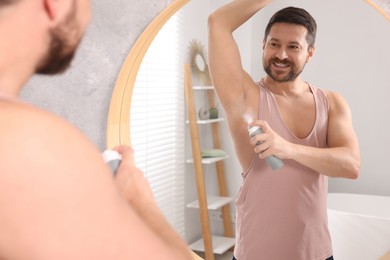 Smiling man applying spray deodorant near mirror at home