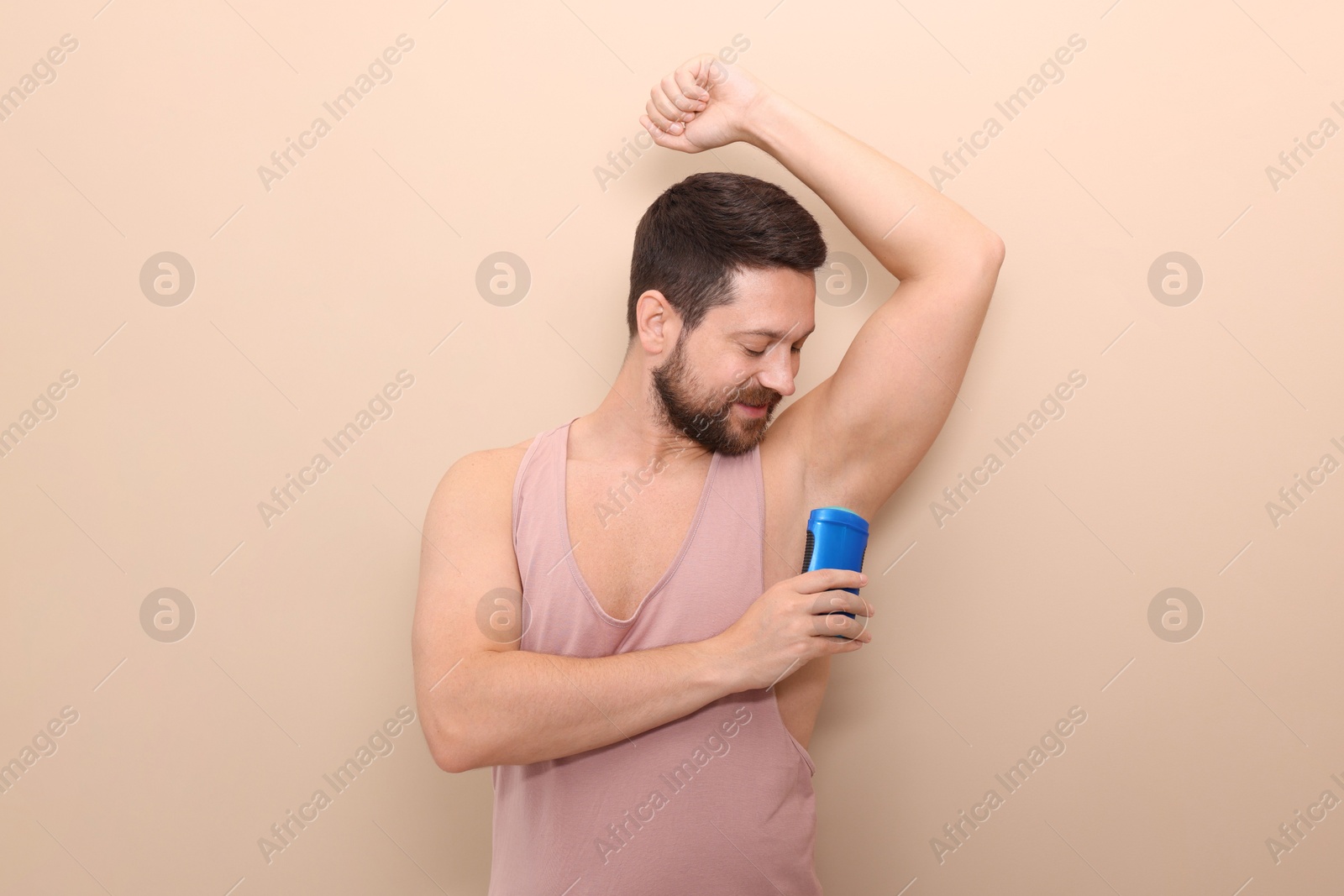 Photo of Man applying solid deodorant on beige background