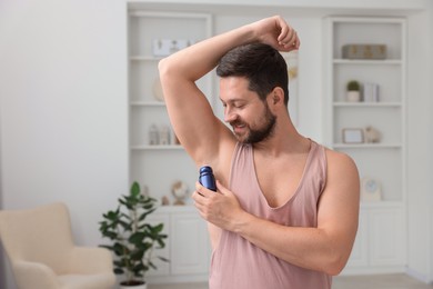 Photo of Man applying roll-on deodorant at home. Space for text