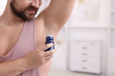 Photo of Man applying roll-on deodorant at home, closeup. Space for text