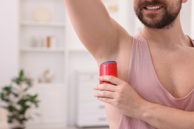 Photo of Smiling man applying solid deodorant at home, closeup. Space for text