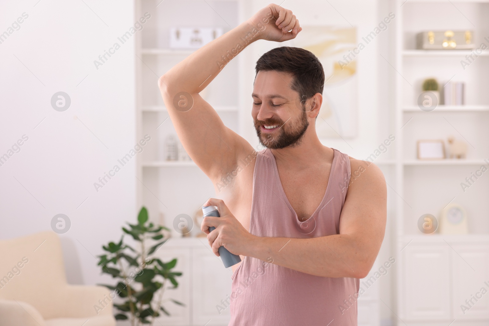 Photo of Smiling man applying spray deodorant at home