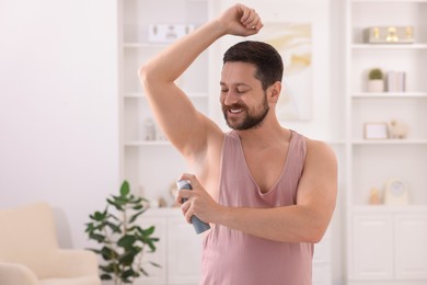 Smiling man applying spray deodorant at home