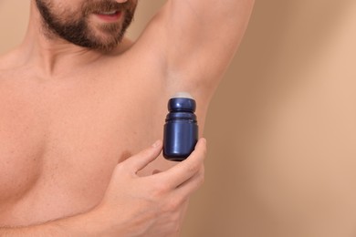 Man applying roll-on deodorant on beige background, closeup. Space for text