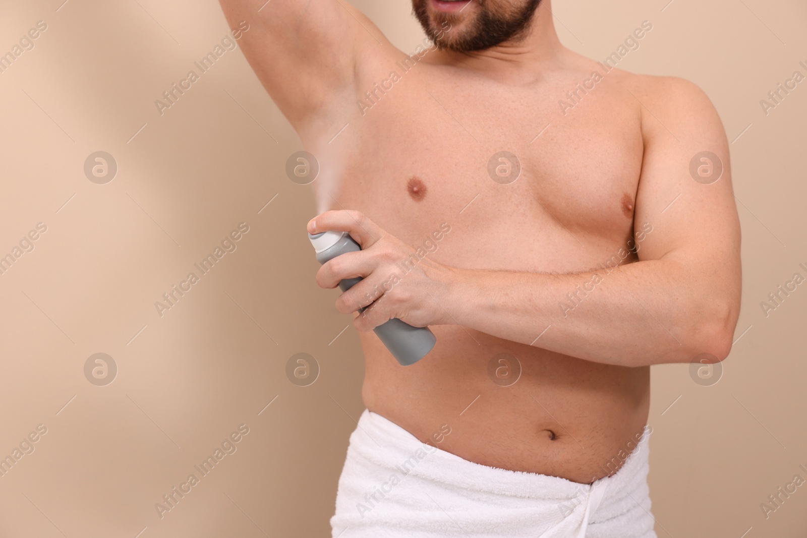 Photo of Man applying spray deodorant on beige background, closeup. Space for text