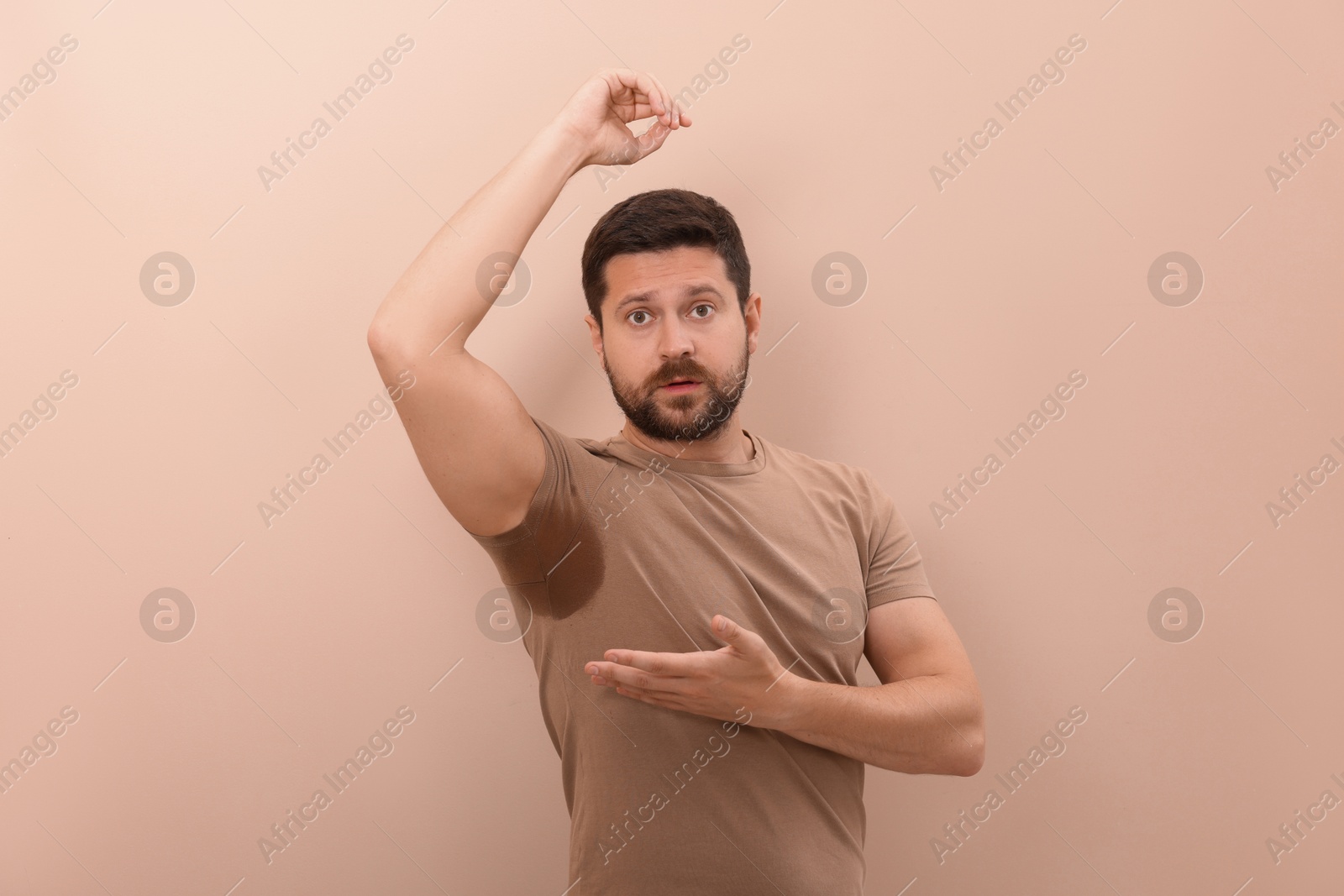 Photo of Emotional man in t-shirt before using deodorant on beige background