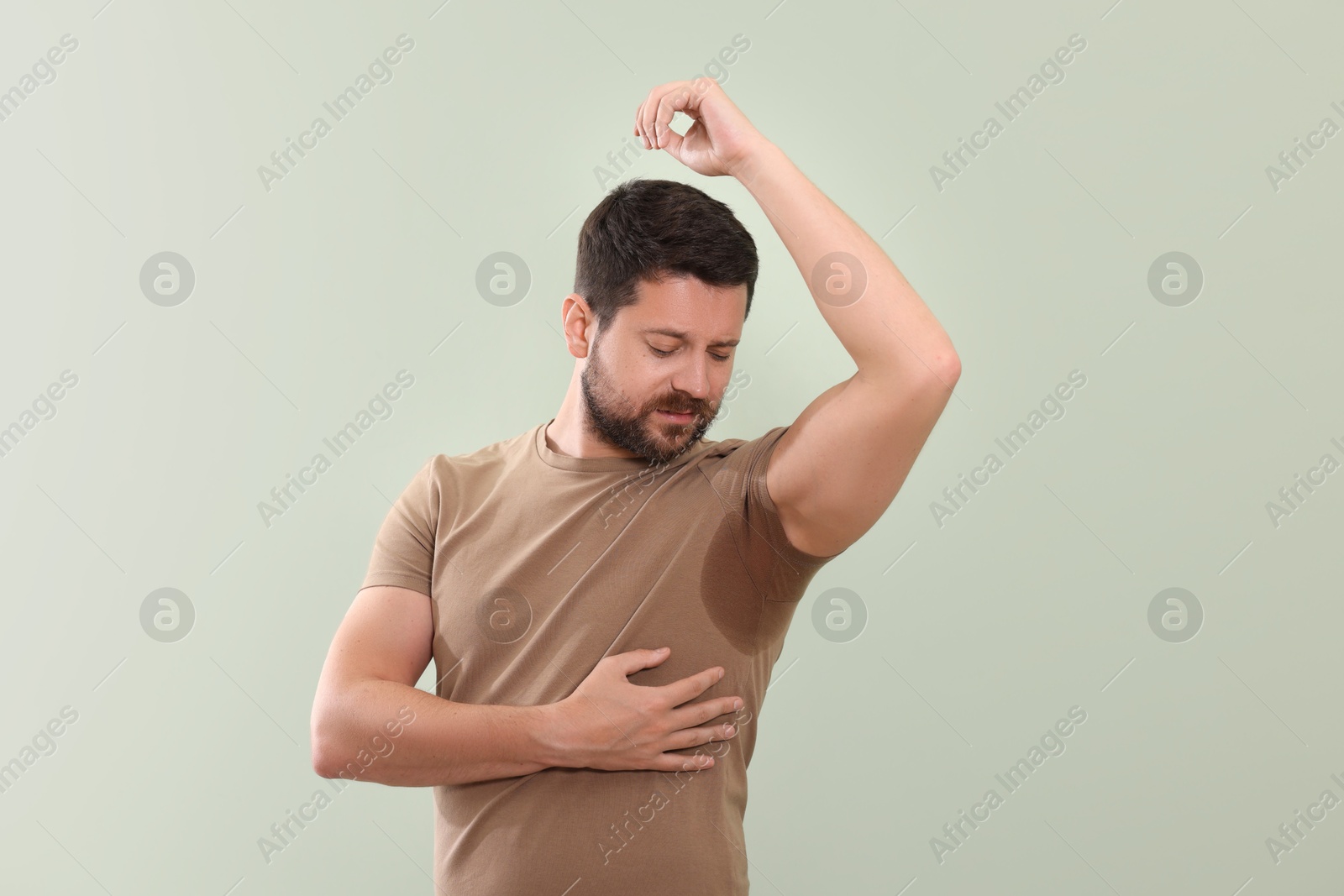 Photo of Emotional man in t-shirt before using deodorant on light green background