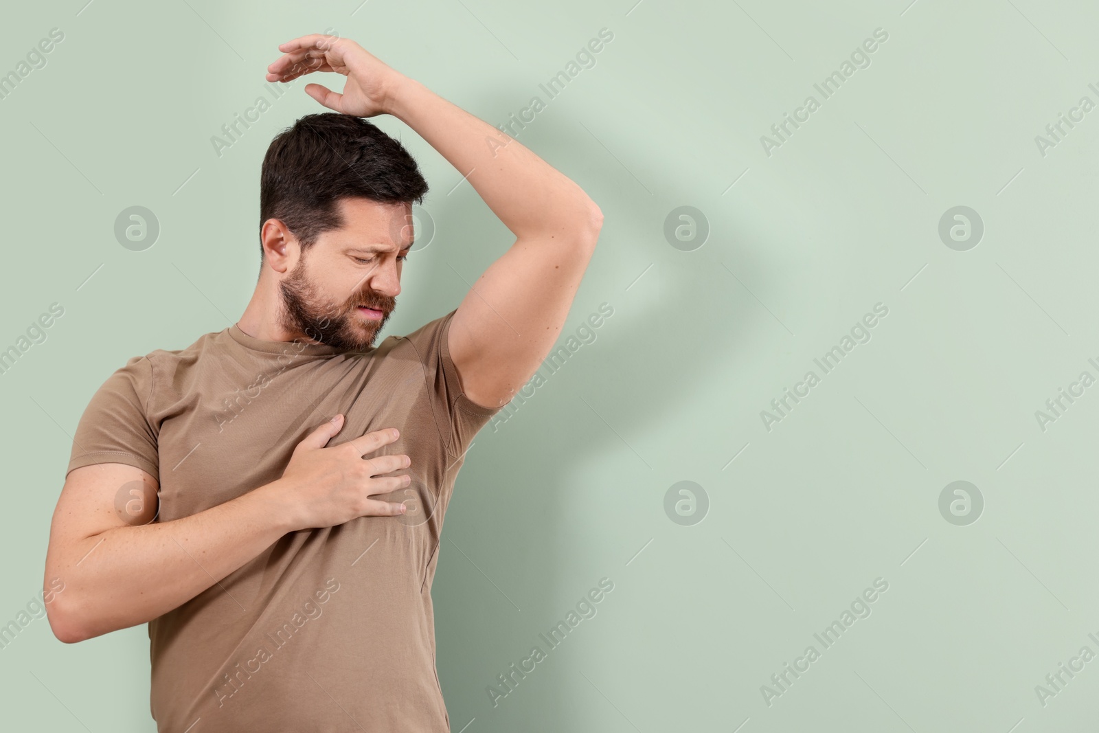 Photo of Emotional man in t-shirt before using deodorant on light green background. Space for text