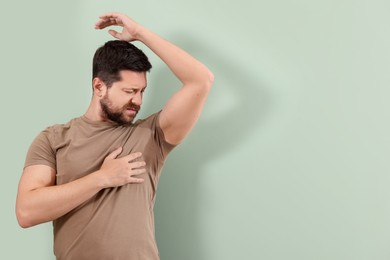 Photo of Emotional man in t-shirt before using deodorant on light green background. Space for text