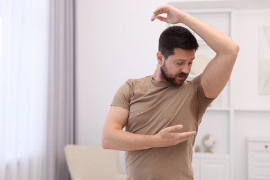 Photo of Emotional man in t-shirt before using deodorant at home. Space for text