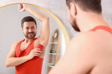 Smiling man applying solid deodorant near mirror at home