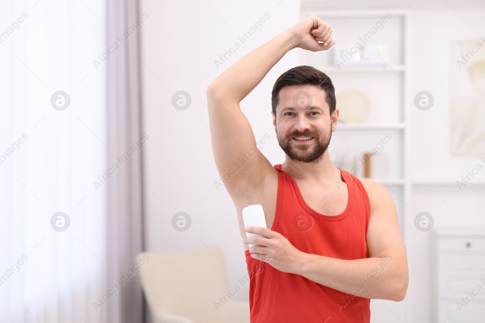 Photo of Smiling man applying solid deodorant at home. Space for text