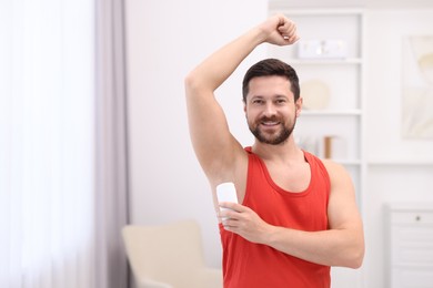 Photo of Smiling man applying solid deodorant at home. Space for text