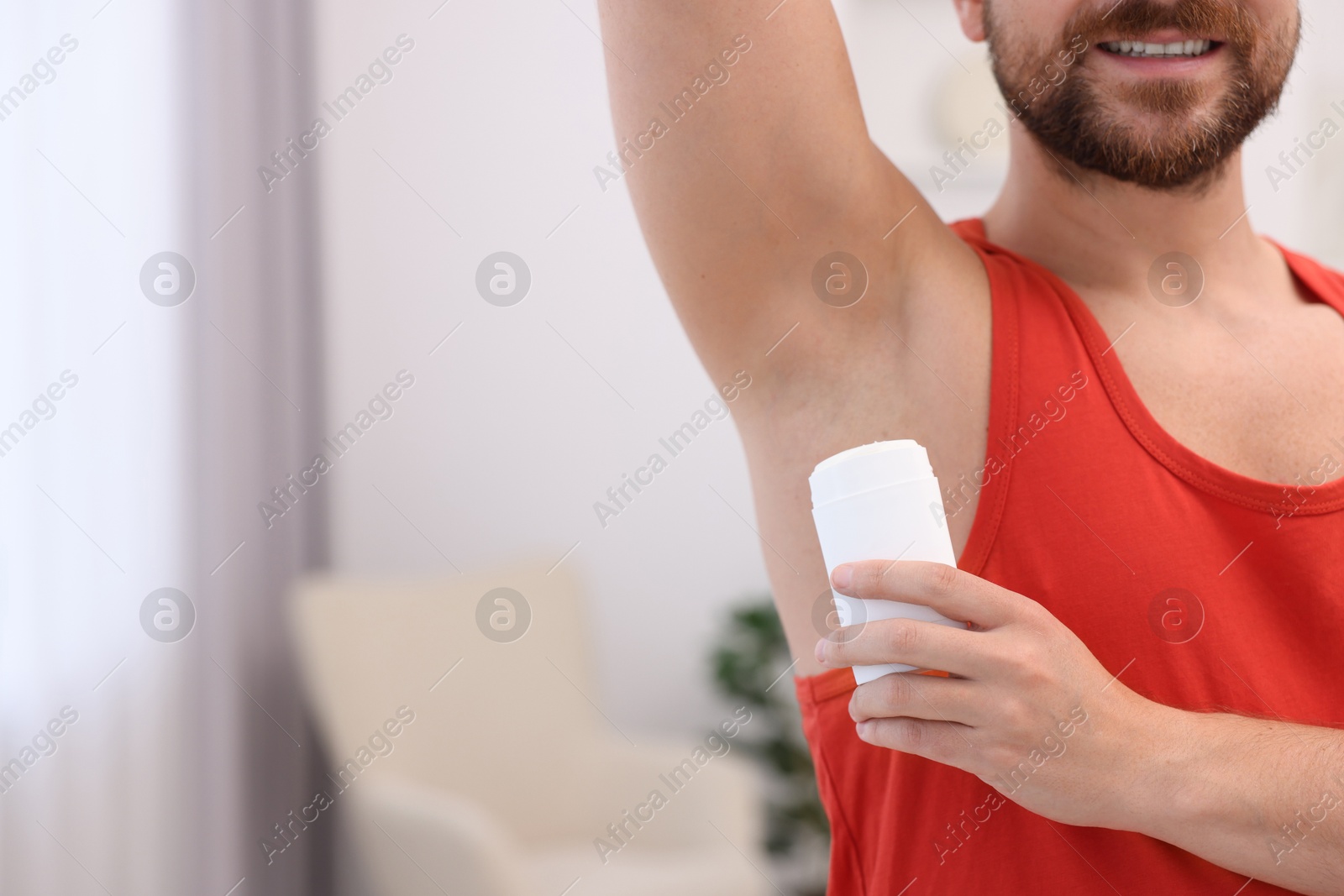 Photo of Smiling man applying solid deodorant at home, closeup. Space for text